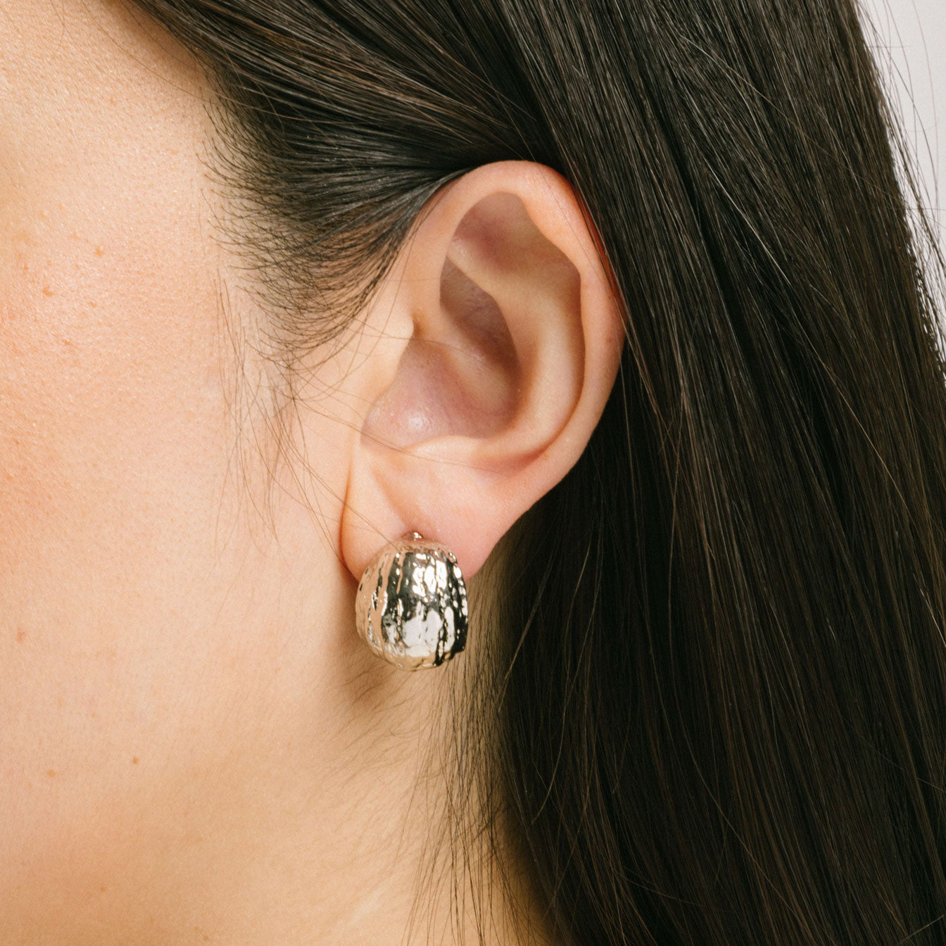 A model wearing the Alaia Clip On Earrings in Silver feature a padded clip-on closure, offering secure hold and ideal comfort for 8-12 hours of wear, for ear types of all shapes and sizes. Crafted from gold tone copper alloy, these earrings feature a single pair per item.