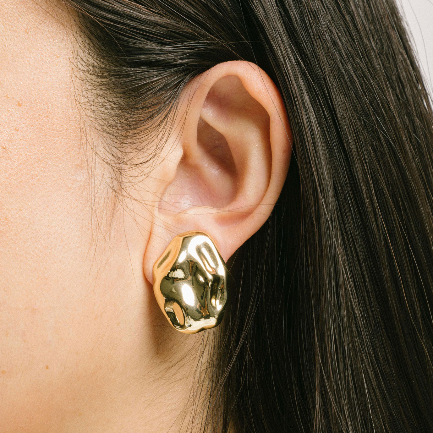 A model wearing the Amaya Clip On Earrings in Gold feature a secure padded clip-on closure type, making them suitable for all ear types.The average comfortable wear duration is 8-12 hours, and the Copper Alloy construction ensures a reliable and secure hold. The item is sold as one pair; adjustable rubber padding is included.