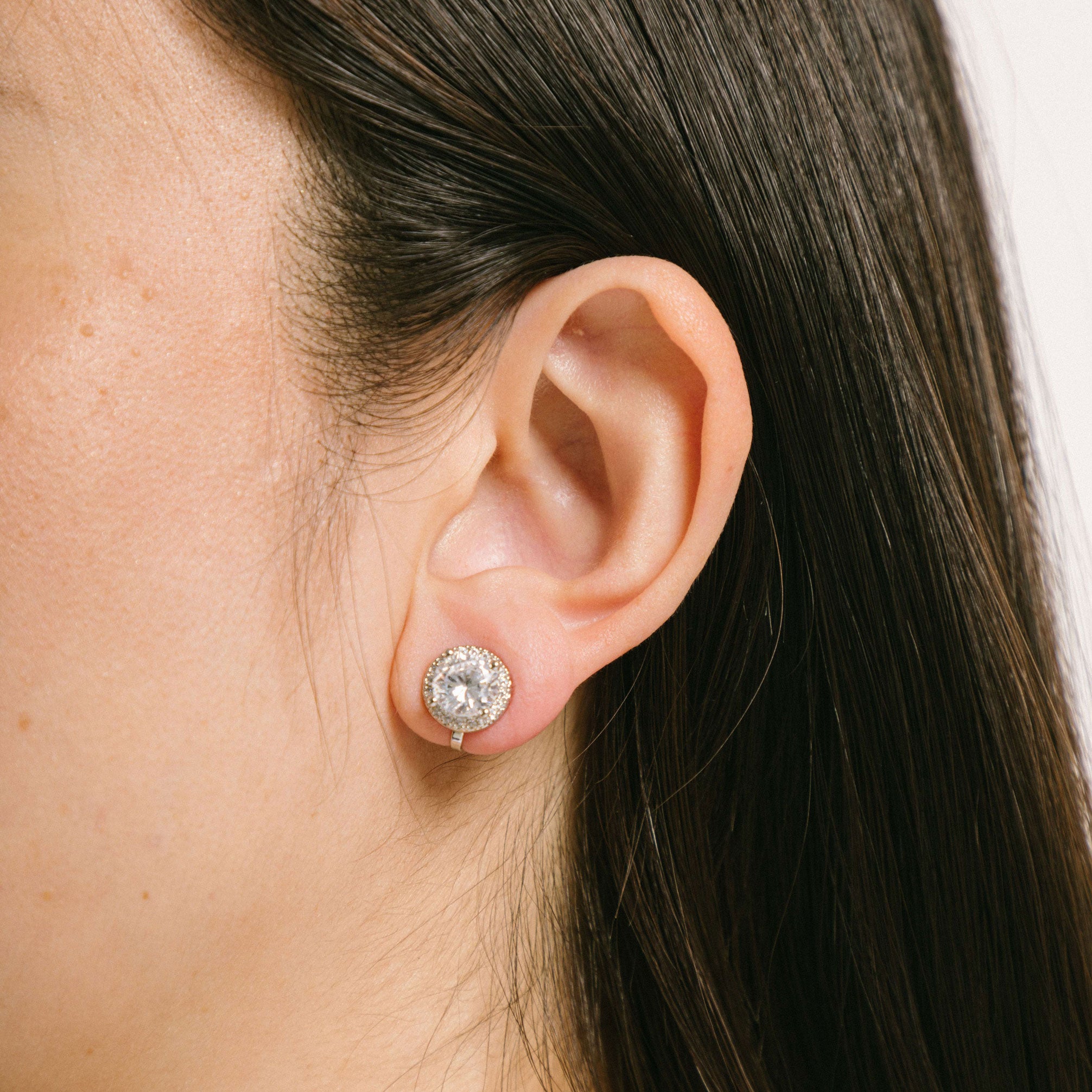 A model wearing the Harper Stud clip-on earrings features a secure hold, with a maximum comfortable wear duration of 8 to 12 hours. It is ideal for all ear types, including thick/large, sensitive, small/thin, and stretched/healing types. It is made with a silver-tone copper alloy and cubic zirconia, and comes with a removable rubber padding for added comfort. Please note: only one pair is included.