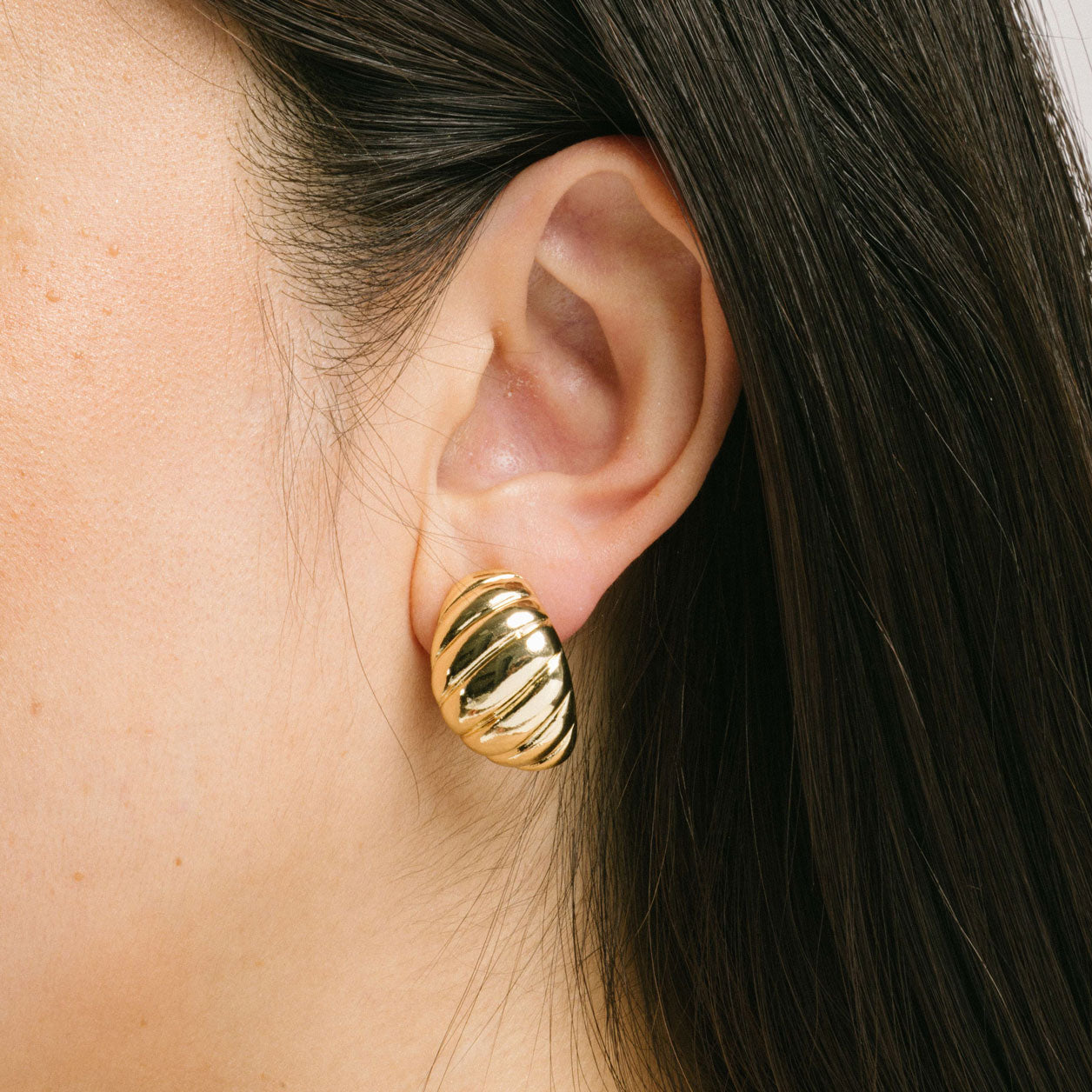 A model wearing the Croissant Dome Clip On Earrings in Gold are designed to provide a secure fit for all ear types. The rubber padding has a comfortable wear duration of 8-12 hours and is made with a Gold Tone Zinc Alloy. This item includes one pair.