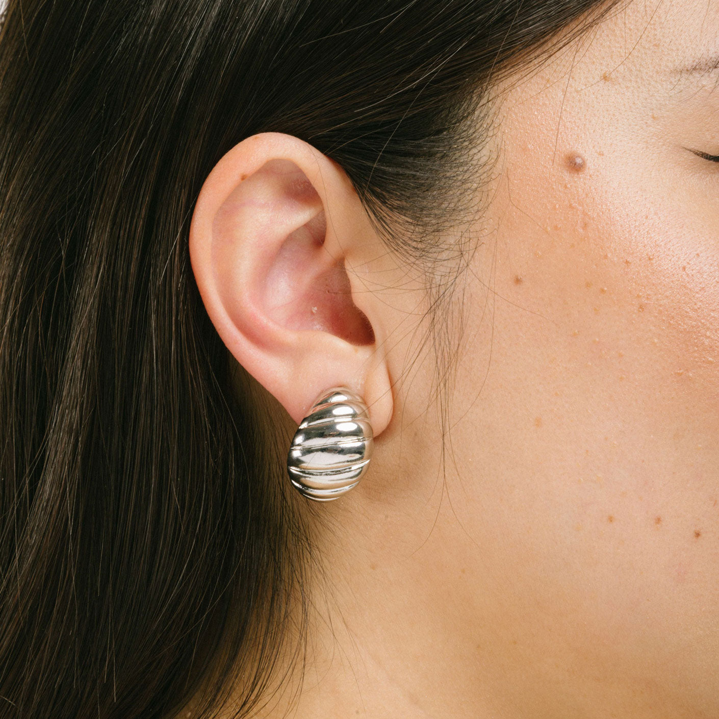 A model wearing the Croissant Dome Clip On Earrings in Silver are designed to provide a secure fit for all ear types. The rubber padding has a comfortable wear duration of 8-12 hours and is made with a Gold Tone Zinc Alloy. This item includes one pair.