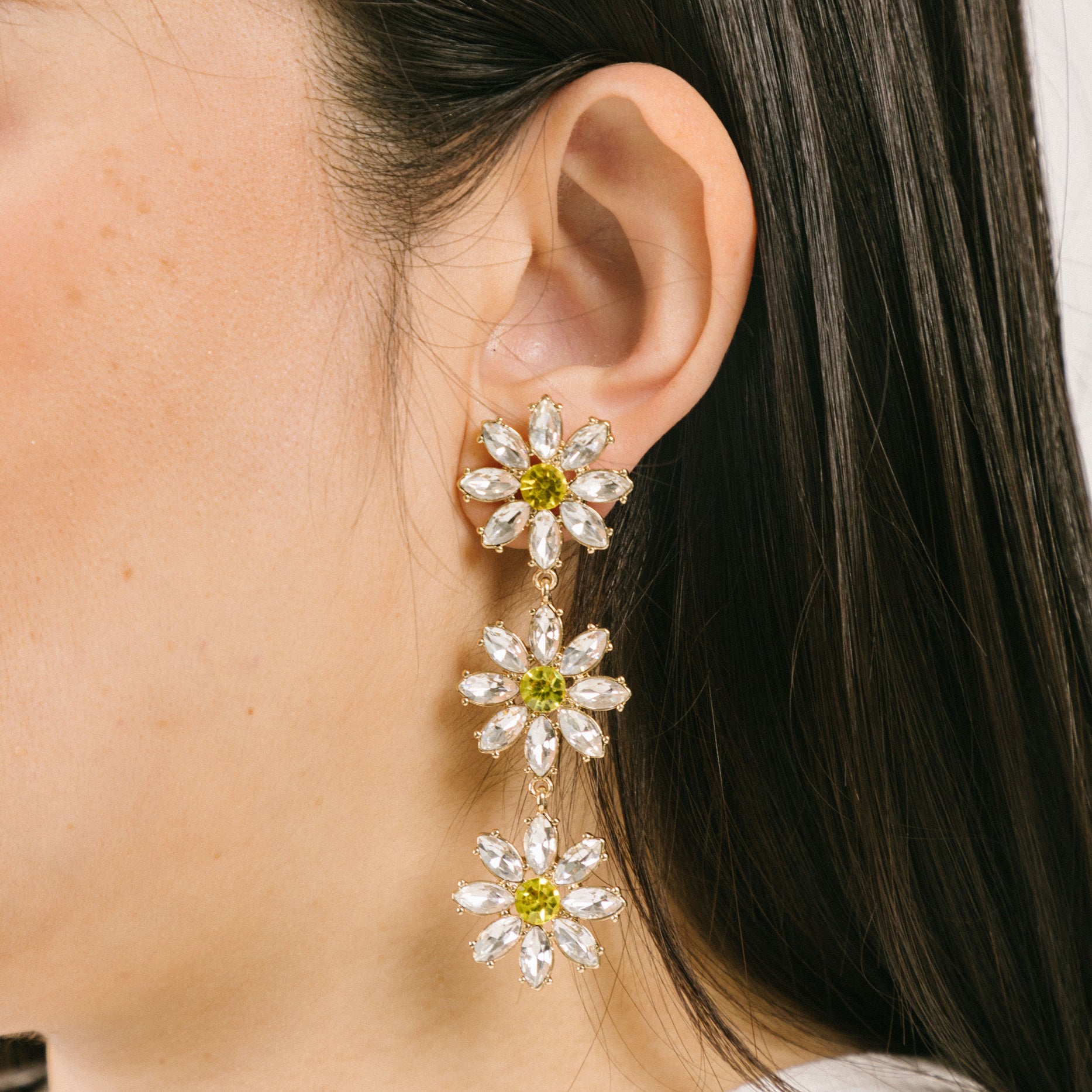 A model wearing the Crystal Flower Drop Clip On Earrings feature a Padded Clip-On closure, perfect for ears of larger proportions as the earrings are on the heavier side. Constructed of gold tone copper alloy and Rhinestone, with detachable rubber padding for added comfort, these earrings provide up to 8-12 hours of easy wear. Sold as one single pair.