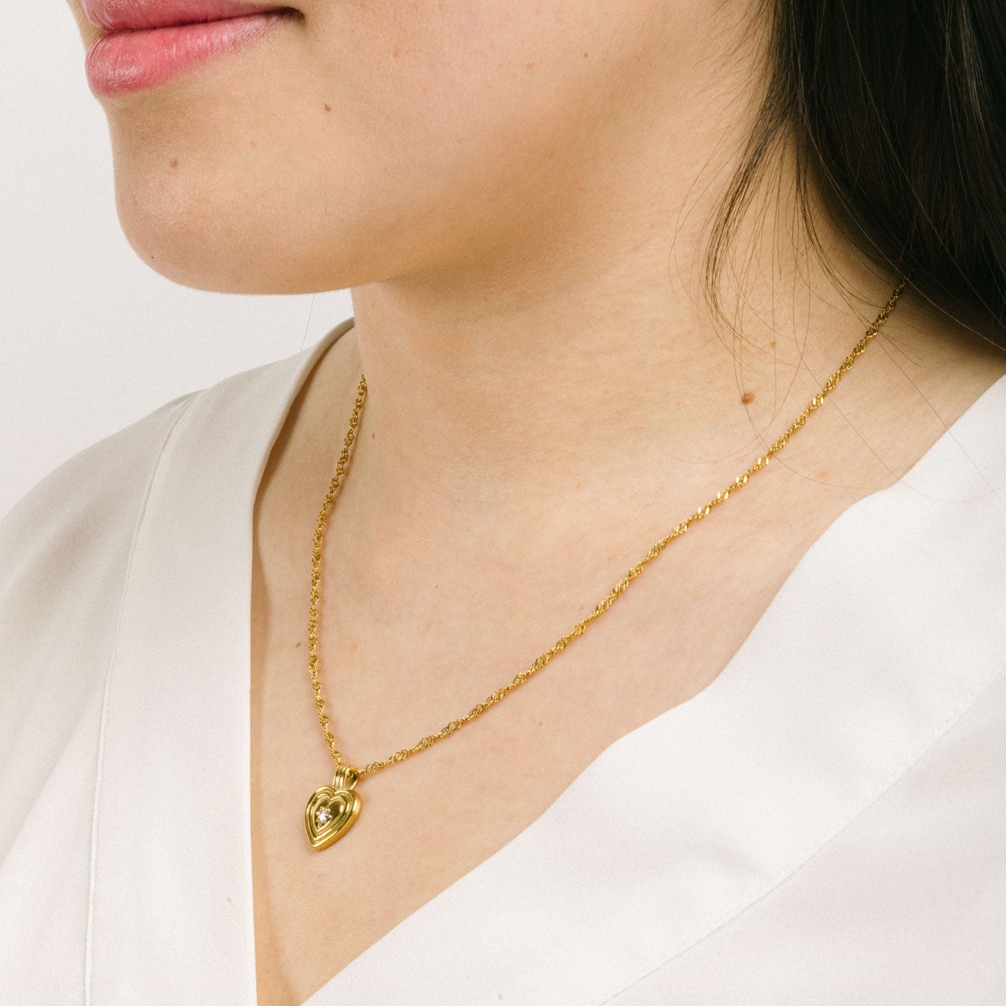 A model wearing the Ellie Heart Pendant Necklace is crafted from 14K Gold Plated Stainless Steel and embellished with Cubic Zirconia. It is adjustable and non-tarnish with great water and allergy resistance.