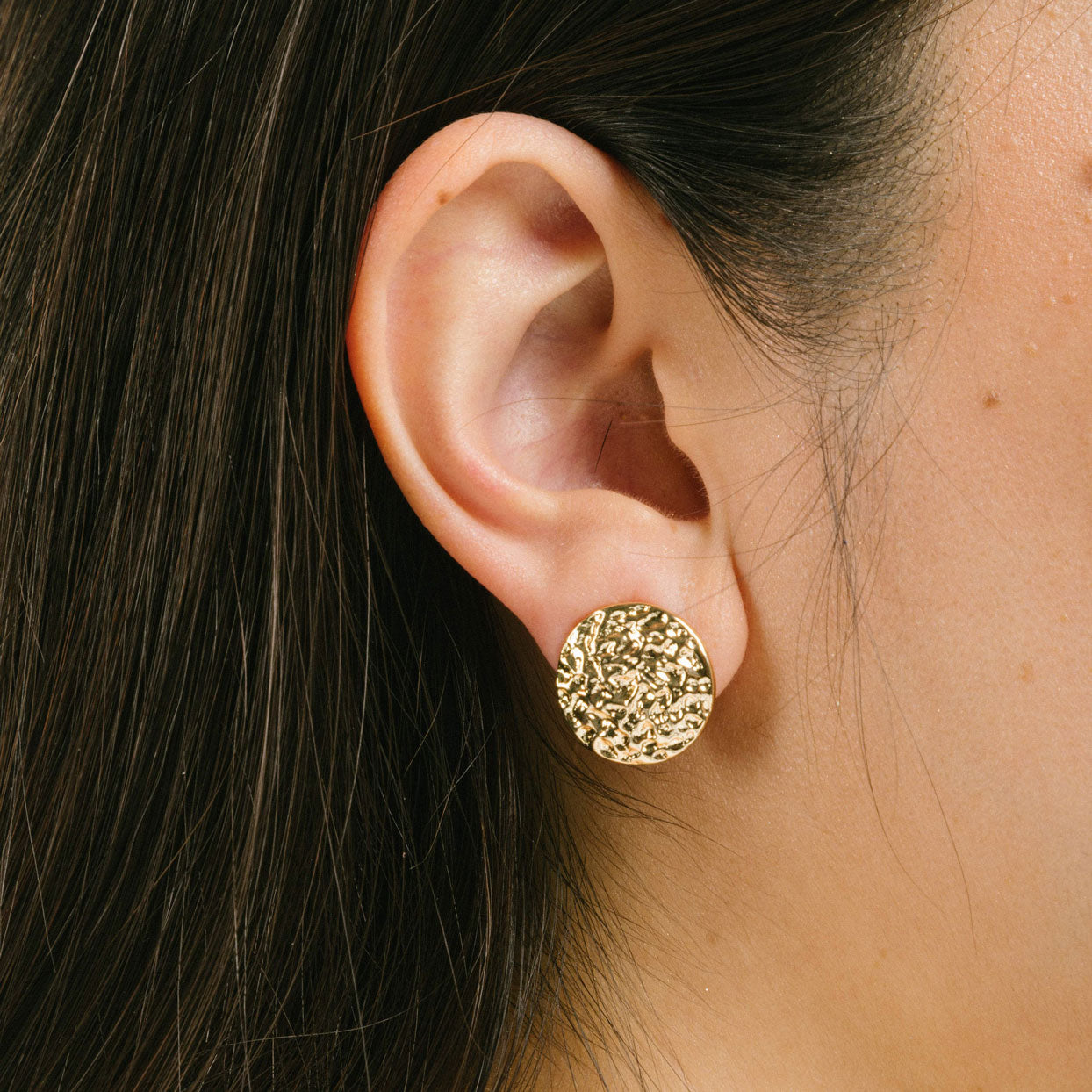 A model wearing the Paloma Clip-On Earrings in Gold provide a secure fit that is perfect for all ear types, including thick/large ears, sensitive ears, small/ thin ears, and stretched/healing ears. These earrings are crafted with a copper alloy and are free of lead and nickel. Their removable rubber padding ensures comfortable wear for up to 12 hours. This package contains one pair of earrings.