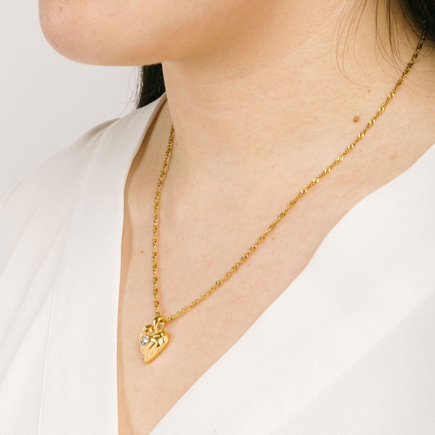 A model wearing the Textured Heart Pendant Necklace is crafted from 14K Gold Plated Stainless Steel with a Cubic Zirconia stone, and is non-tarnish, water resistant, and free from Lead, Nickel, and Cadmium. It is also adjustable and has only one necklace included.