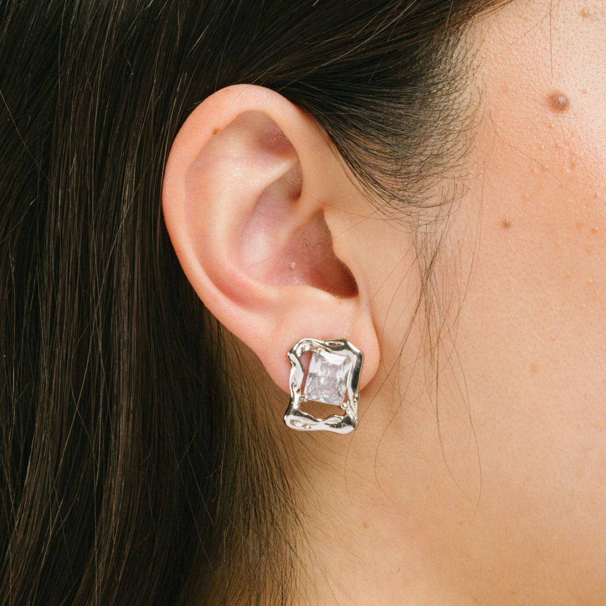 A model wearing the Valerie Clip On Earrings in Silver offer a secure hold for up to 12 hours of comfortable wear. Featuring a padded clip-on design, these earrings are ideal for all ear types, including those that are thick and large, sensitive, small and thin, or stretched and healing. Crafted with a silver tone copper alloy and cubic zirconia, each order includes one pair.