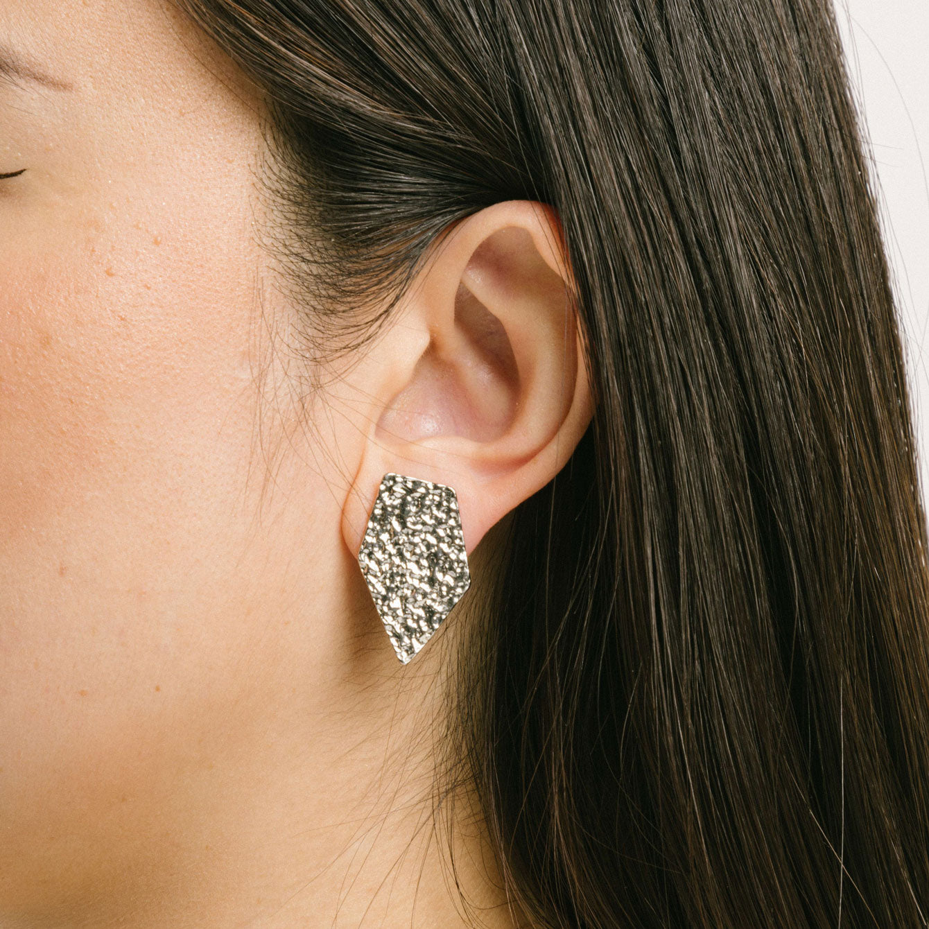 A model wearing the Vesper Clip On Earrings in Silver are padded clip-on earrings with a secure hold. Perfect for all ear types, they offer a comfortable wear for 8-12 hours. Made of zinc and copper alloy, the earrings come with a removable black rubber padding and can be worn as pictured. Please note, item is sold as one pair.