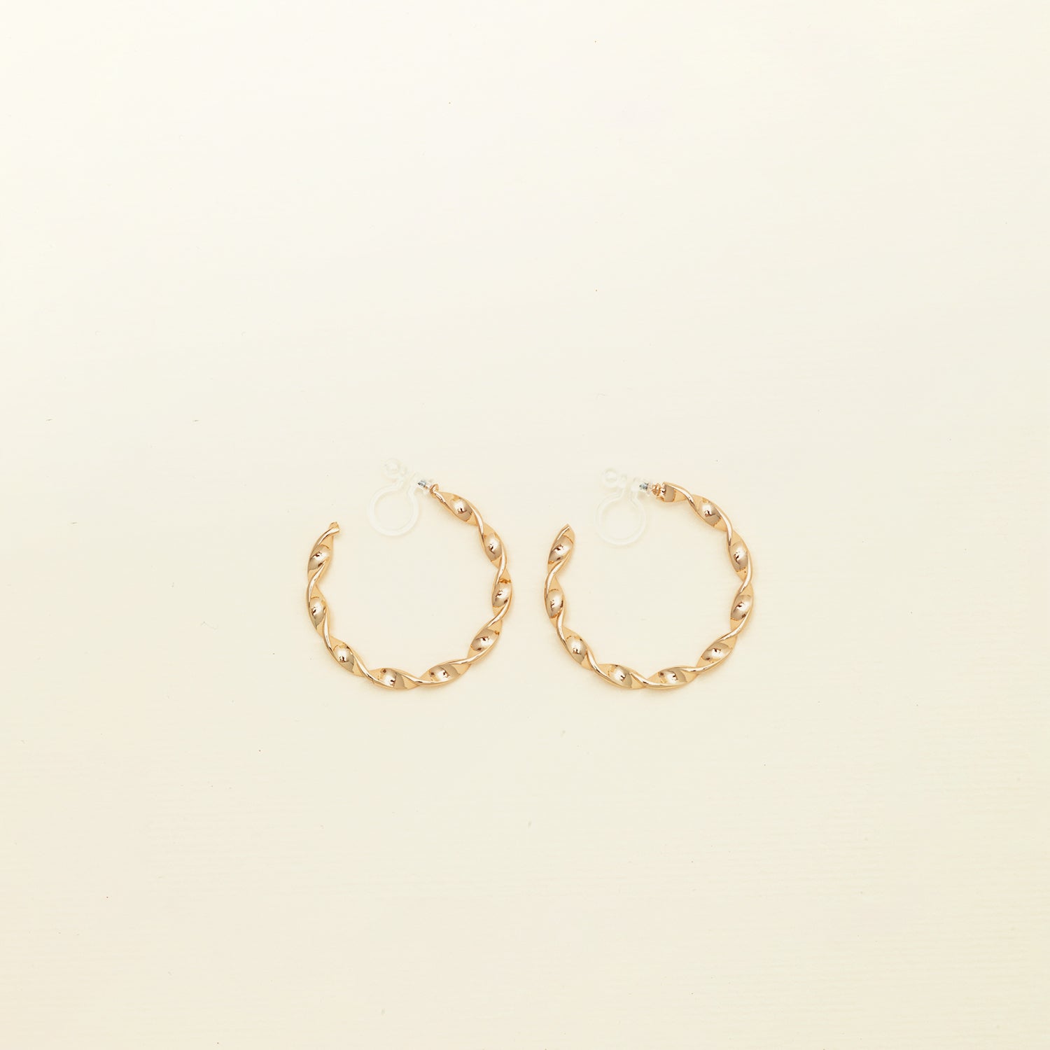 Image of the Gold Wave Hoop Clip-On Earrings boast a closure type of resin clip-on, ideal for the vast majority of ear types. Average wear duration ranges from 8-12 hours, offering medium secure hold with no ability to adjust. Crafted from gold tone metal alloy, this item comes as one pair and is also available in silver.