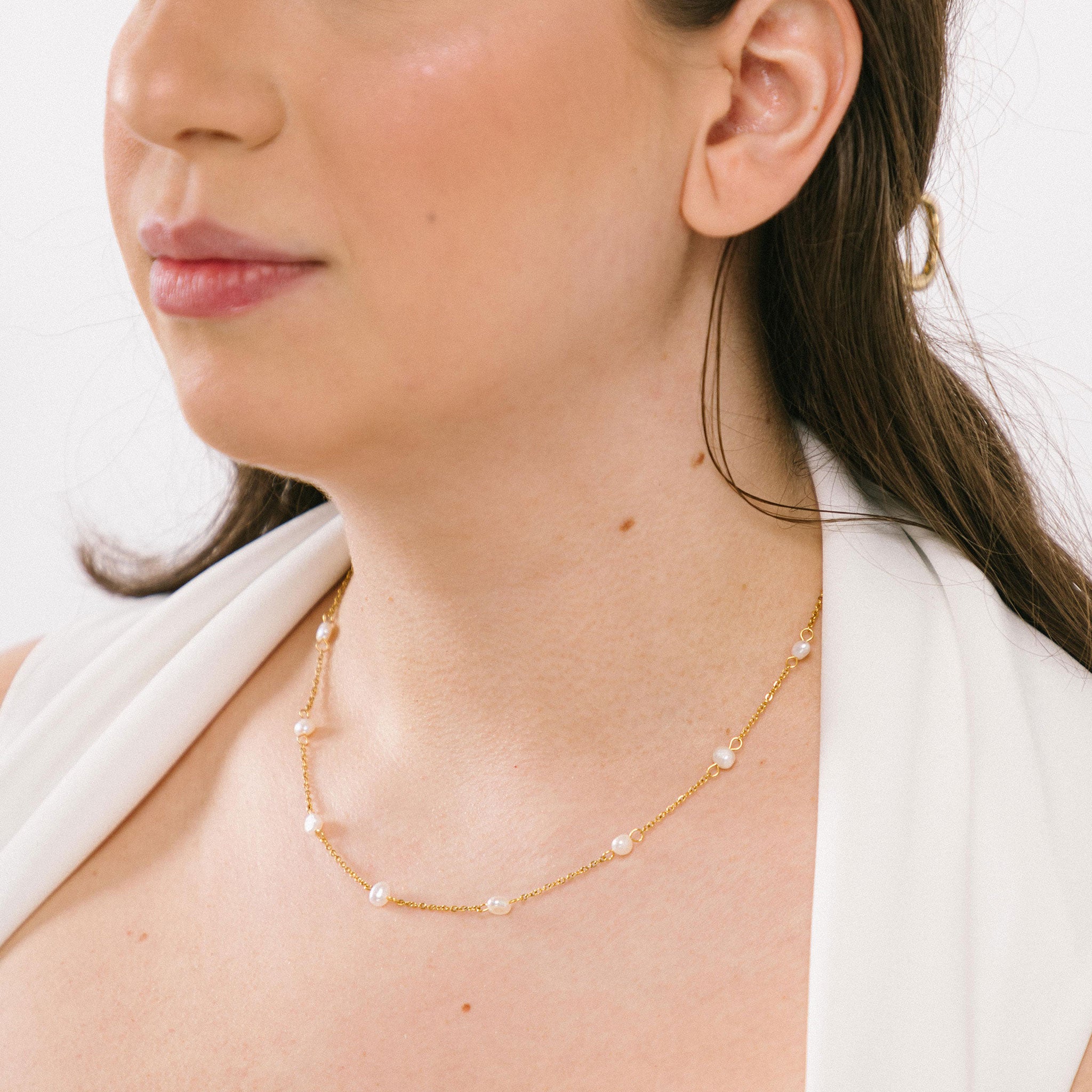 A model wearing the Elena Pearl Necklace is adjustable and crafted from Freshwater Pearls, 18K Gold Plated Stainless Steel, and is waterproof and hypoallergenic. Each pearl may vary slightly in size and colour due to its natural characteristics.