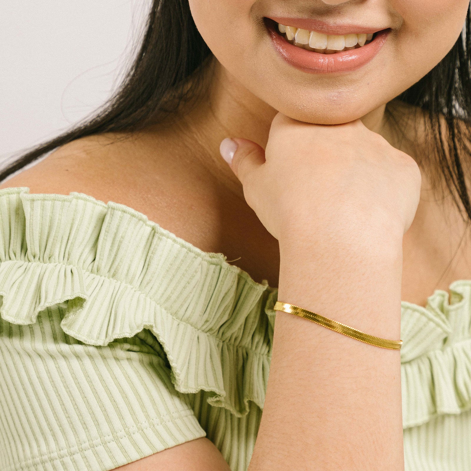 A model wearing the Herringbone Chain Bracelet is crafted with 18K Gold Plated on 316L Stainless Steel, making it non-tarnish, water resistant, nickel-free, and hypoallergenic. It has an adjustable feature, but it is sold as a single bracelet.