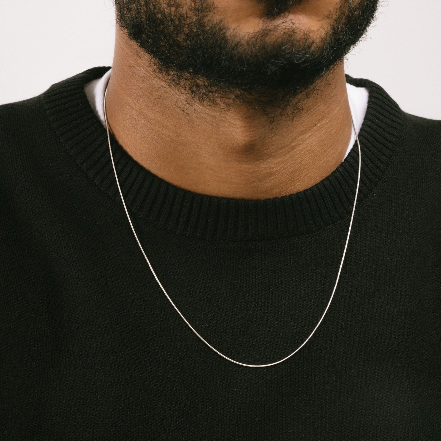 A model wearing the 1mm Snake Chain is made of durable stainless steel, measuring 22 inches in length. It's also non-tarnish and water-resistant for extra protection.