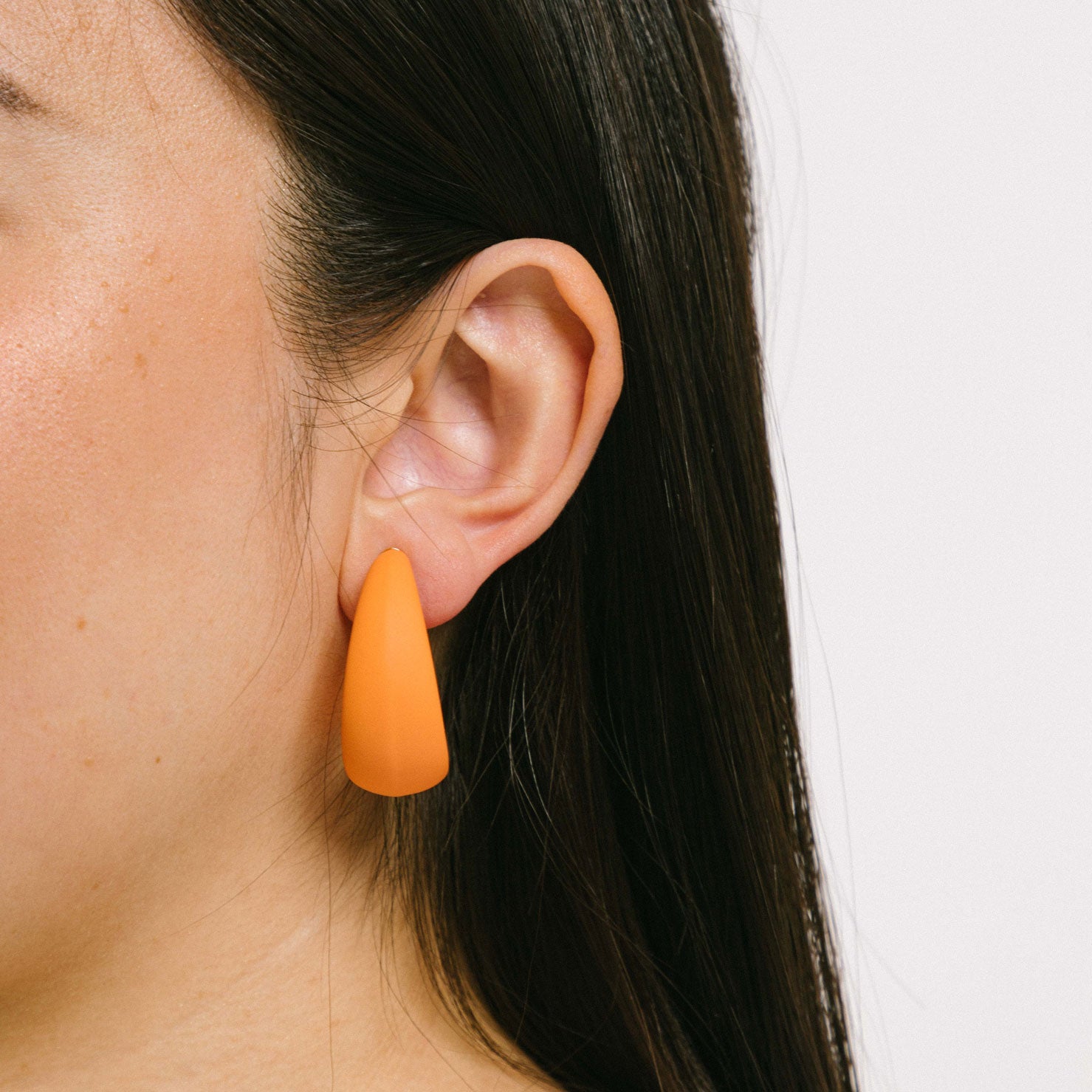 Fashionable model showcasing orange clip-on earrings with screwback closure, providing a secure hold for all ear types. These earrings can be manually adjusted to ensure a perfect fit. 