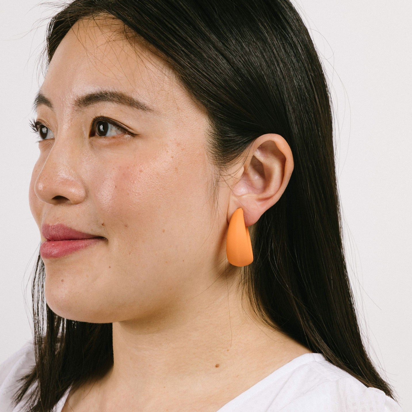 Model wearing stylish orange screwback clip-on earrings, ideal for various ear types. These earrings offer a secure hold and manual adjustment for personalized comfort. Crafted from gold tone copper metal alloy and acrylic. 