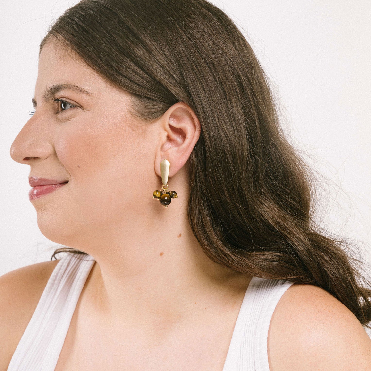A model wear trendy brown clip-on hoop earrings offering a secure hold for all ear types. Agate and glass bead elements complement the matte gold tone copper alloy. Clip-On earring with removable rubber padding.