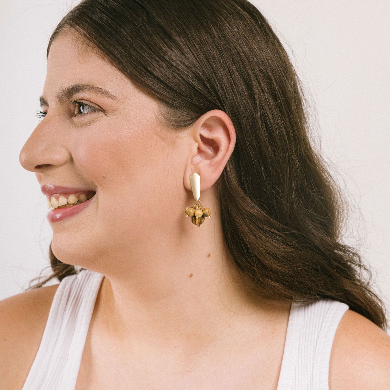 Model rocking a trendy light brown clip-on earrings. The matte gold tone copper alloy earrings feature agate and glass bead details. Securely fastened with padded closures, perfect for all ear types.