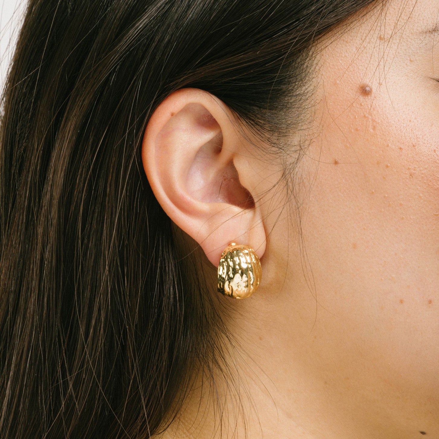 A model wearing the Alaia Clip On Earrings in Gold feature a padded clip-on closure, offering secure hold and ideal comfort for 8-12 hours of wear, for ear types of all shapes and sizes. Crafted from gold tone copper alloy, these earrings feature a single pair per item.