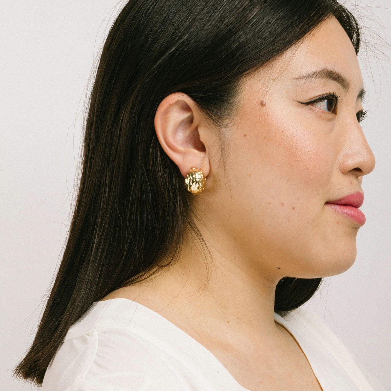 A model wearing the Alaia Clip On Earrings in Gold feature a padded clip-on closure, offering secure hold and ideal comfort for 8-12 hours of wear, for ear types of all shapes and sizes. Crafted from gold tone copper alloy, these earrings feature a single pair per item.