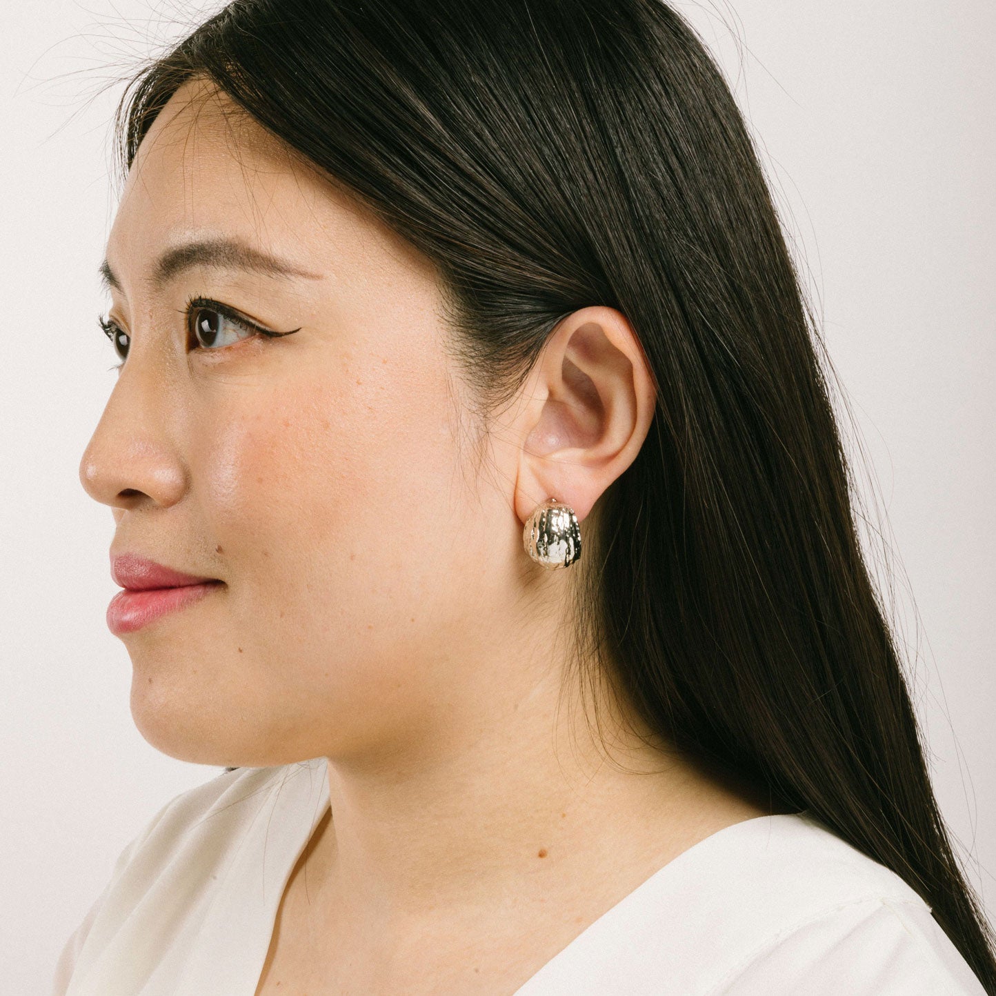 A model wearing the Alaia Clip On Earrings in Silver feature a padded clip-on closure, offering secure hold and ideal comfort for 8-12 hours of wear, for ear types of all shapes and sizes. Crafted from gold tone copper alloy, these earrings feature a single pair per item.