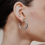 A model wearing the Allie Hoop Clip On Earrings in Silver, which are perfect for all ear types. The Mosquito Coil Clip-On Closure is suitable for Thick/Large, Sensitive, Small/Thin, Stretched/Healing, and Keloid Prone Ears. Made of a silver tone copper alloy, each purchase includes one pair.