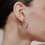 A model wearing the Allie Hoop Clip On Earrings in Silver, which are perfect for all ear types. The Mosquito Coil Clip-On Closure is suitable for Thick/Large, Sensitive, Small/Thin, Stretched/Healing, and Keloid Prone Ears. Made of a silver tone copper alloy, each purchase includes one pair.