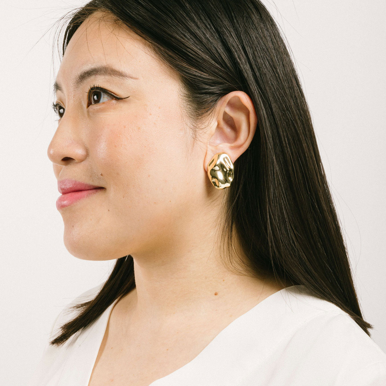 A model wearing the Amaya Clip On Earrings in Gold feature a secure padded clip-on closure type, making them suitable for all ear types.The average comfortable wear duration is 8-12 hours, and the Copper Alloy construction ensures a reliable and secure hold. The item is sold as one pair; adjustable rubber padding is included.