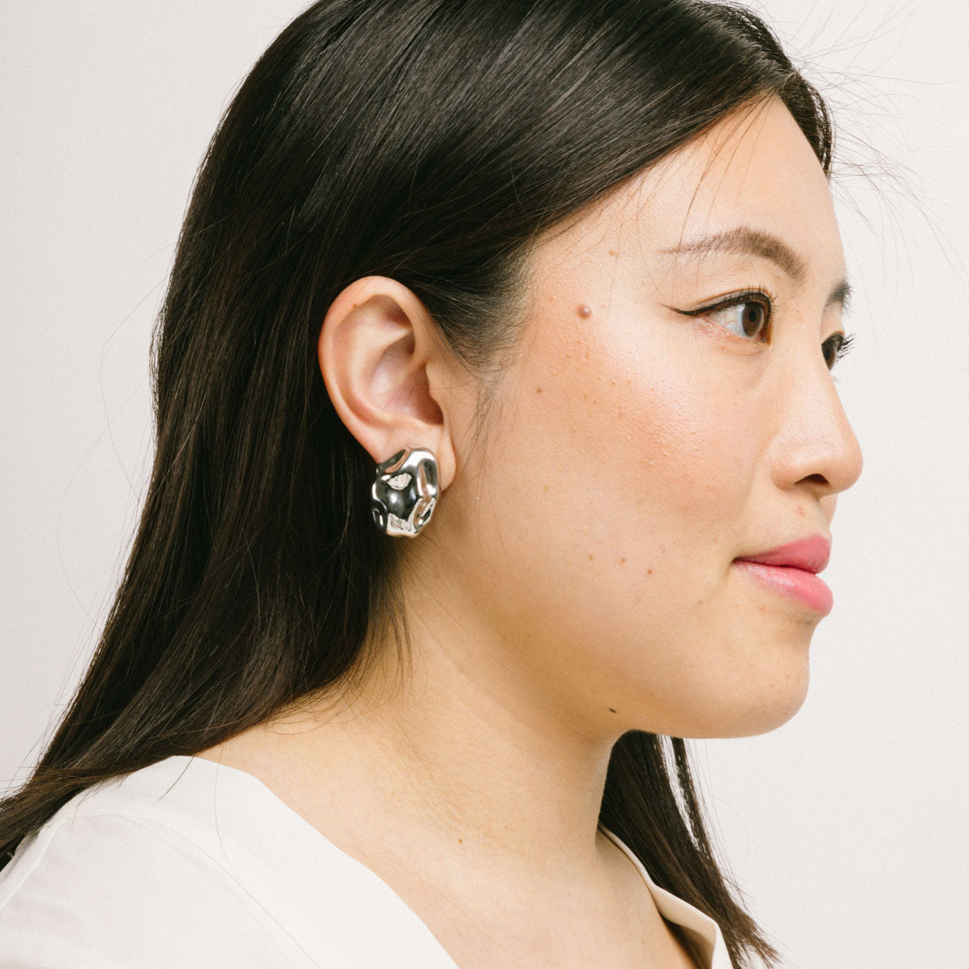 A model wearing the Amaya Clip On Earrings in Silver feature a secure padded clip-on closure type, making them suitable for all ear types.The average comfortable wear duration is 8-12 hours, and the Copper Alloy construction ensures a reliable and secure hold. The item is sold as one pair; adjustable rubber padding is included.