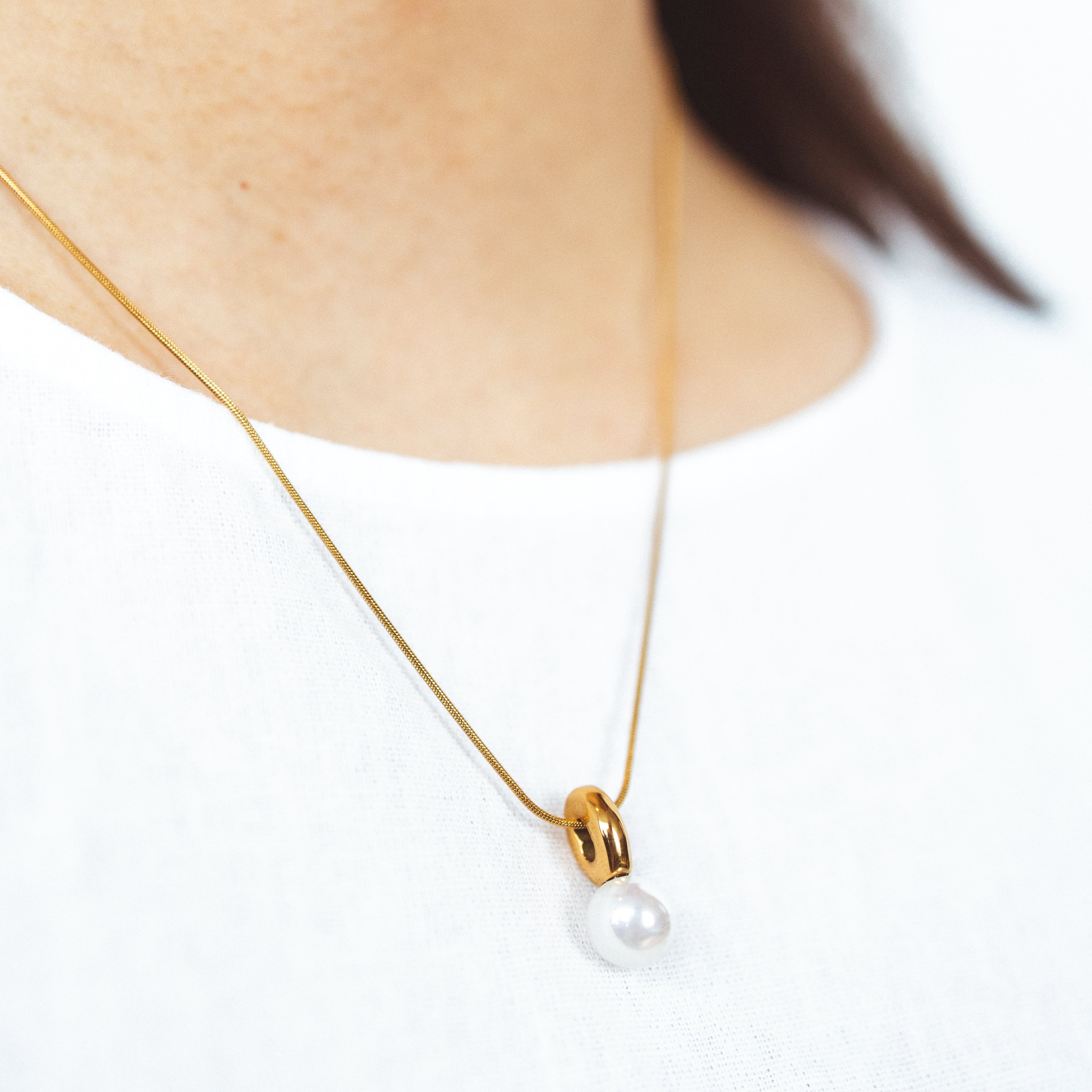 A model wearing the Ariel Pearl Necklace boasts a Mother of Pearl Pendant for a timeless and enduring beauty. Resilient against tarnishing and water, this necklace exudes confidence and sophistication. Perfect for any occasion.