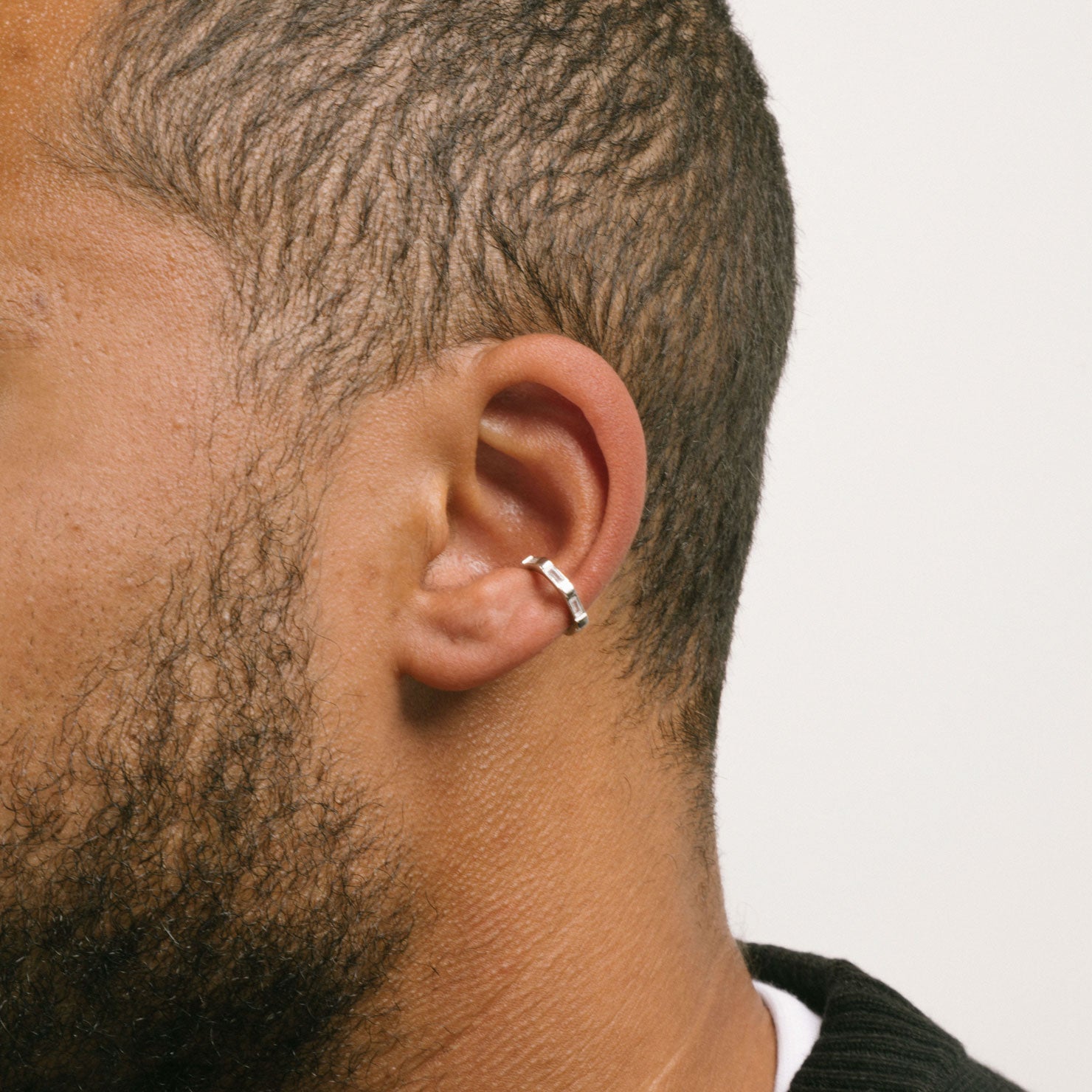 A model wearing the Baguette Gem Ear Cuff features a clip-on closure type ideal for all ear types. The average comfortable wear duration is up to 24 hours at a medium secure hold that can be gently adjusted. The material composition is silver tone plated copper and cubic zirconia. Please note, item is sold as one piece.