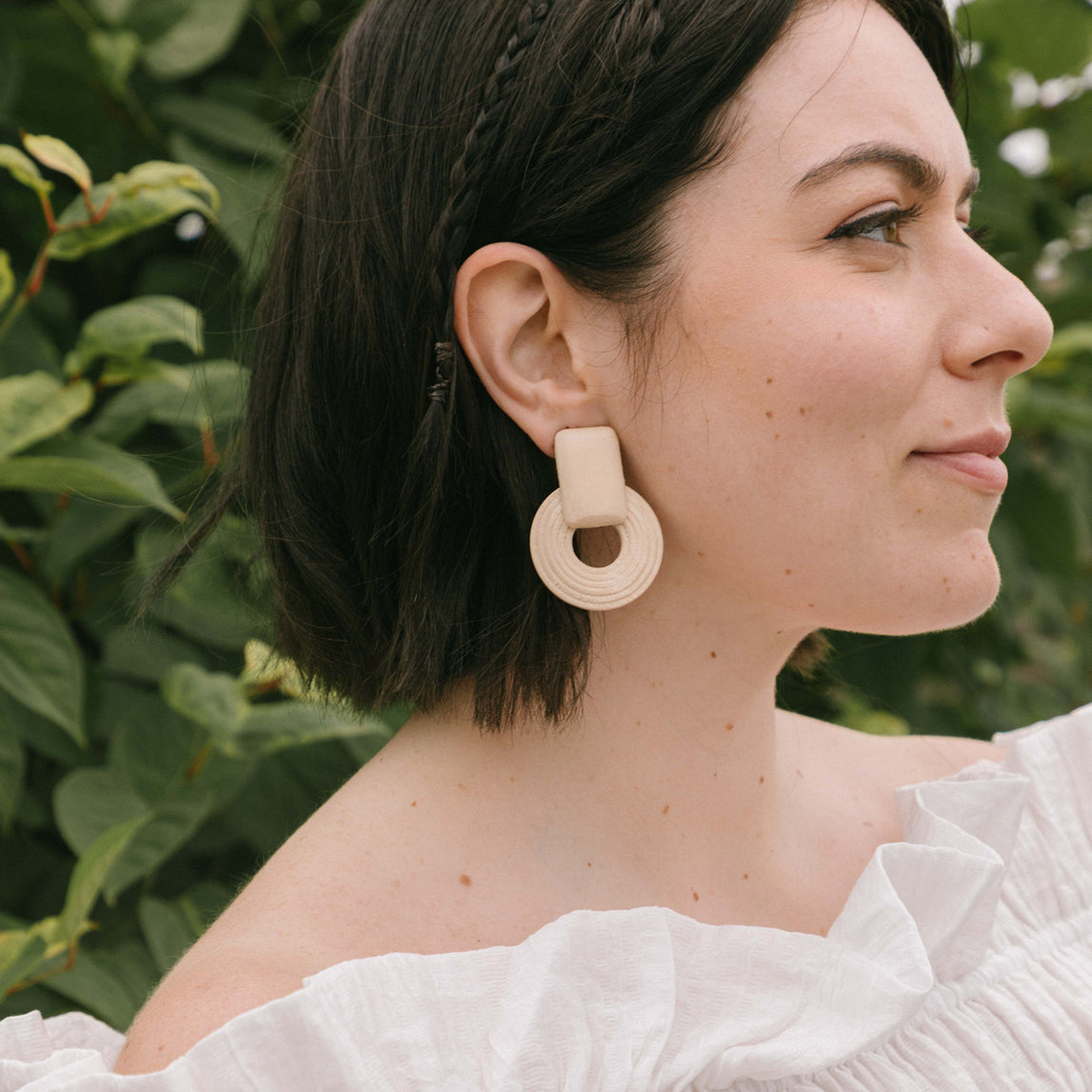 A model wearing the Sand Dune Clip On Earrings provide a secure hold for 8-12 hours, with the ability to adjust to any ear size. Crafted with copper alloy and wood, one pair is included. The screwback clip-on design is ideal for thick/large, sensitive, small/thin, and stretched/healing ear types.