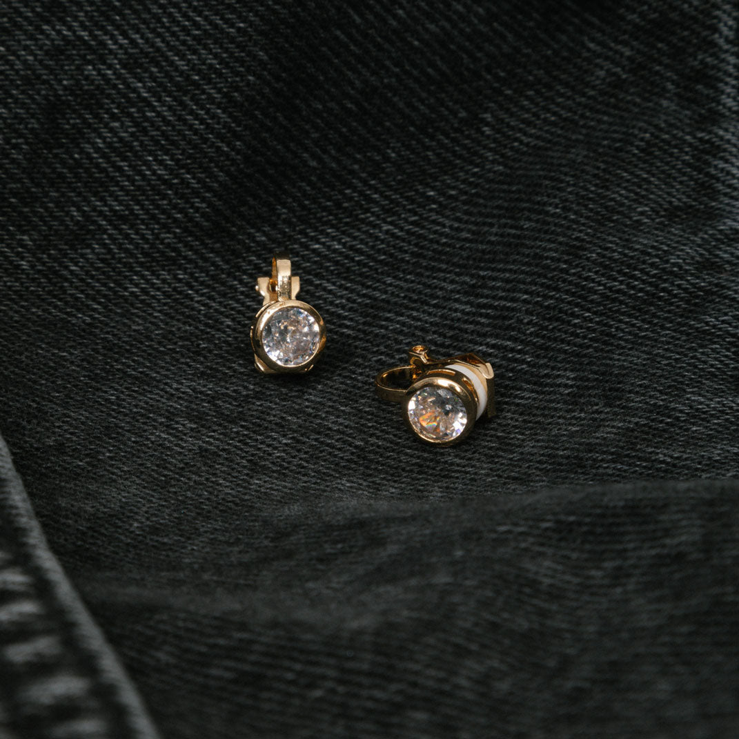 Image of the Bezel Stud Clip-On Earrings in Gold provide a secure hold for up to 12 hours. Made of gold tone plated copper and Cubic Zirconia, these earrings feature a padded closure type that works with all ear types, including thick, large, sensitive, small, thin, and stretched or healing ears. Please note that item being sold is only one pair.