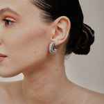 A model wearing the Bold Ribbed Hoop Clip On Earrings in Silver. Our screwback closure and manual adjustment capabilities cater to a wide range of needs, including thick, sensitive, small, and keloid-prone ears. Easily wear them for 8-12 hours for all-day fashion. Sold in pairs.