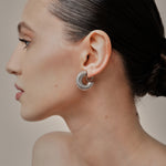 A model wearing the Bold Ribbed Hoop Clip On Earrings in Silver. Our screwback closure and manual adjustment capabilities cater to a wide range of needs, including thick, sensitive, small, and keloid-prone ears. Easily wear them for 8-12 hours for all-day fashion. Sold in pairs.