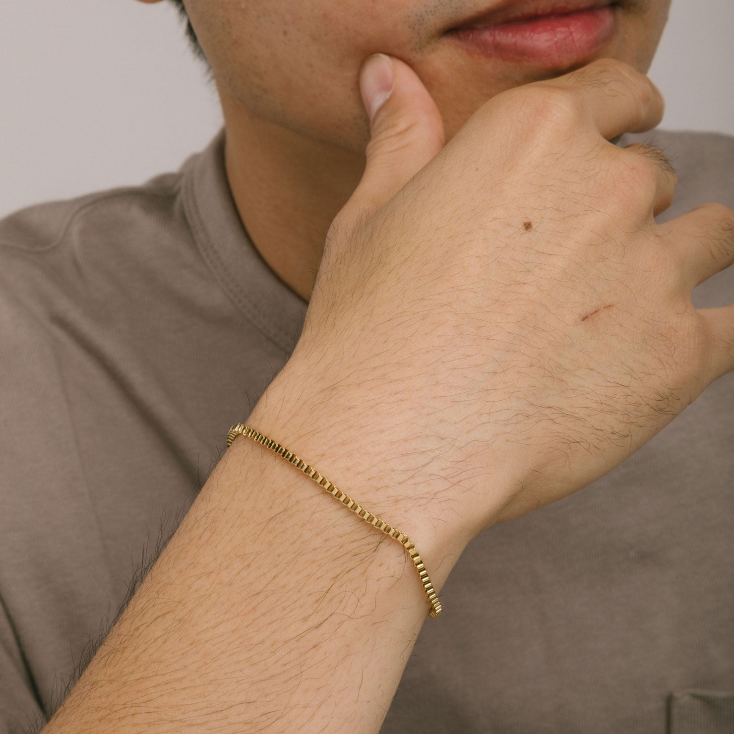 A model wearing the Box Chain Bracelet in Gold is 18K Gold Plated, offering a non-tarnish, water-resistant finish.