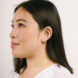 A model wearing the Harper Stud Clip On Earrings in Gold are ideal for any ear type, offering a secure hold for up to 12 hours of comfortable wear. Crafted from gold tone copper alloy and Cubic Zirconia, the earrings feature a padded clip-on closure and removable rubber padding. Please note the item is for one pair only.