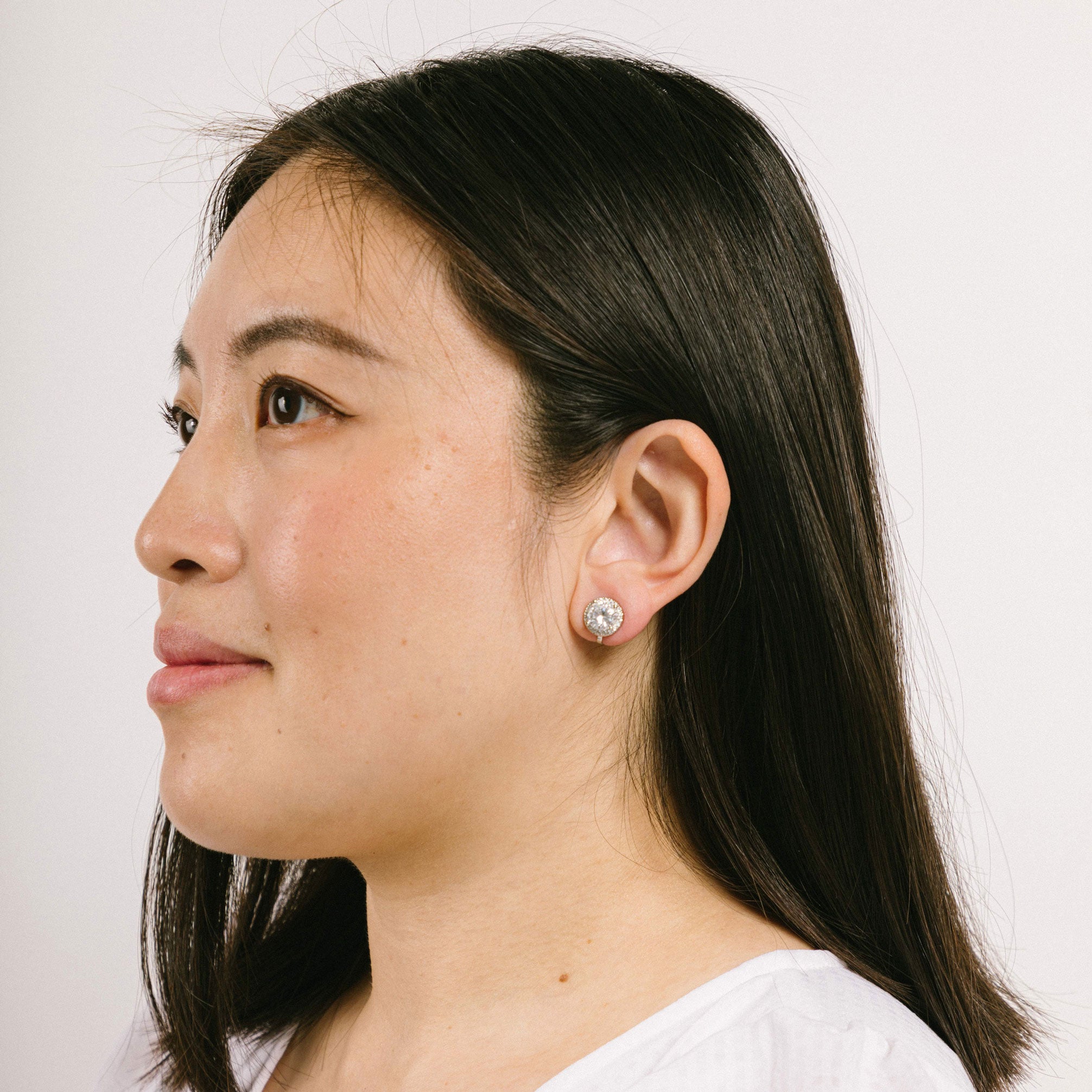 A model wearing the Harper Stud clip-on earrings features a secure hold, with a maximum comfortable wear duration of 8 to 12 hours. It is ideal for all ear types, including thick/large, sensitive, small/thin, and stretched/healing types. It is made with a silver-tone copper alloy and cubic zirconia, and comes with a removable rubber padding for added comfort. Please note: only one pair is included.