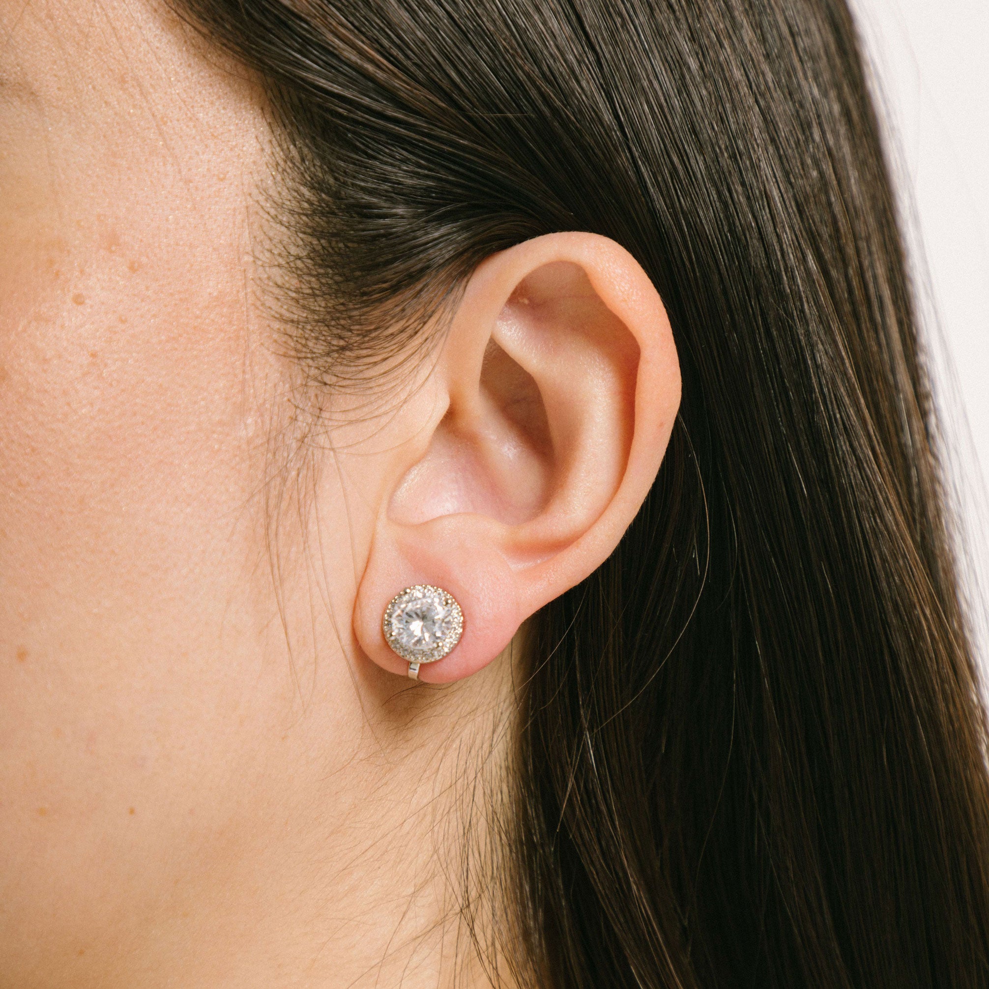 A model wearing the Harper Stud clip-on earrings features a secure hold, with a maximum comfortable wear duration of 8 to 12 hours. It is ideal for all ear types, including thick/large, sensitive, small/thin, and stretched/healing types. It is made with a silver-tone copper alloy and cubic zirconia, and comes with a removable rubber padding for added comfort. Please note: only one pair is included.