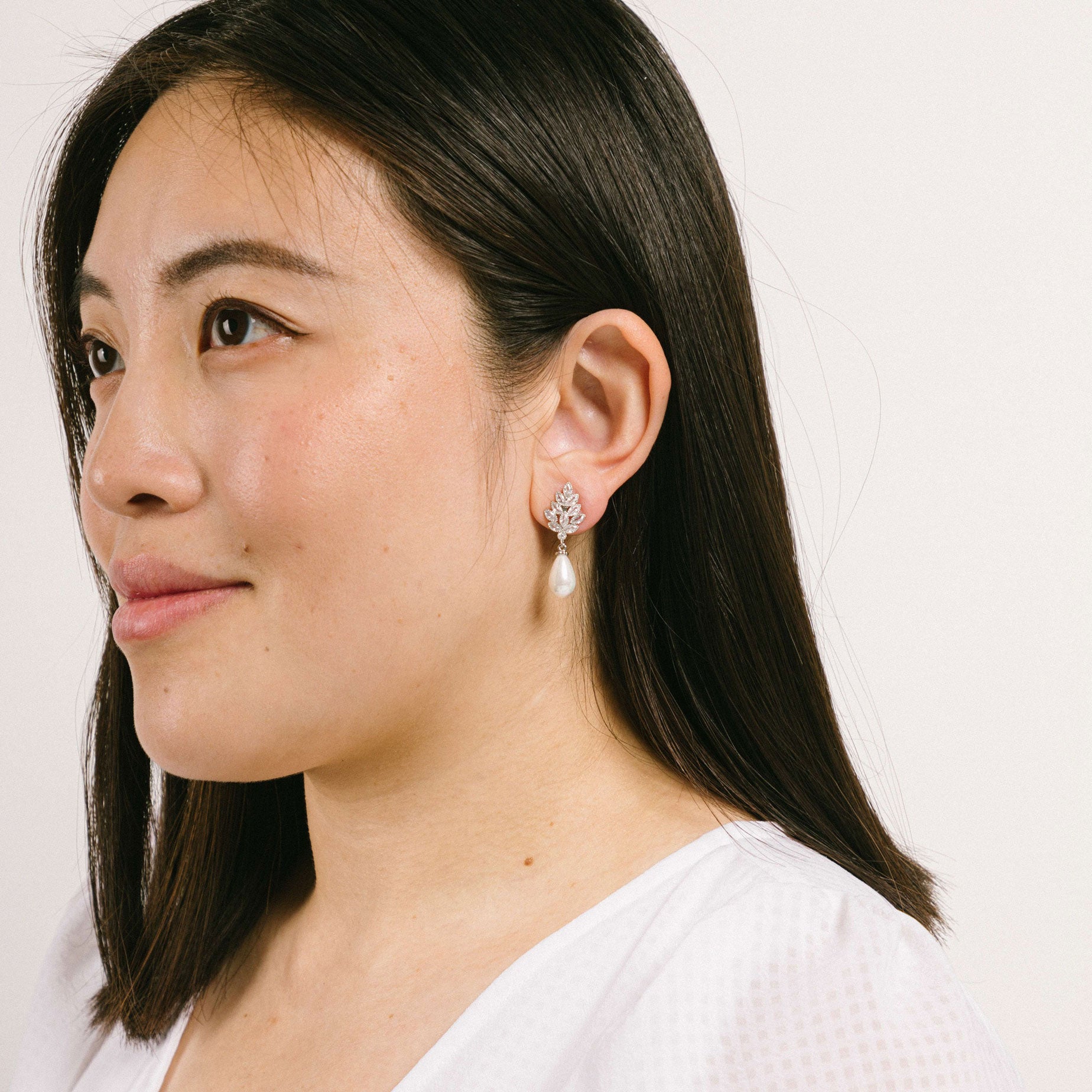 A model wearing the Madeline Clip On Earrings feature comfortable, secure and stylish padded clips ideal for all ear types. With a strong, consistent hold that can last up to 8-12 hours, they feature silver plated copper alloy with Cubic Zirconia and Simulated Pearl accents. This product is sold singularly as one pair.