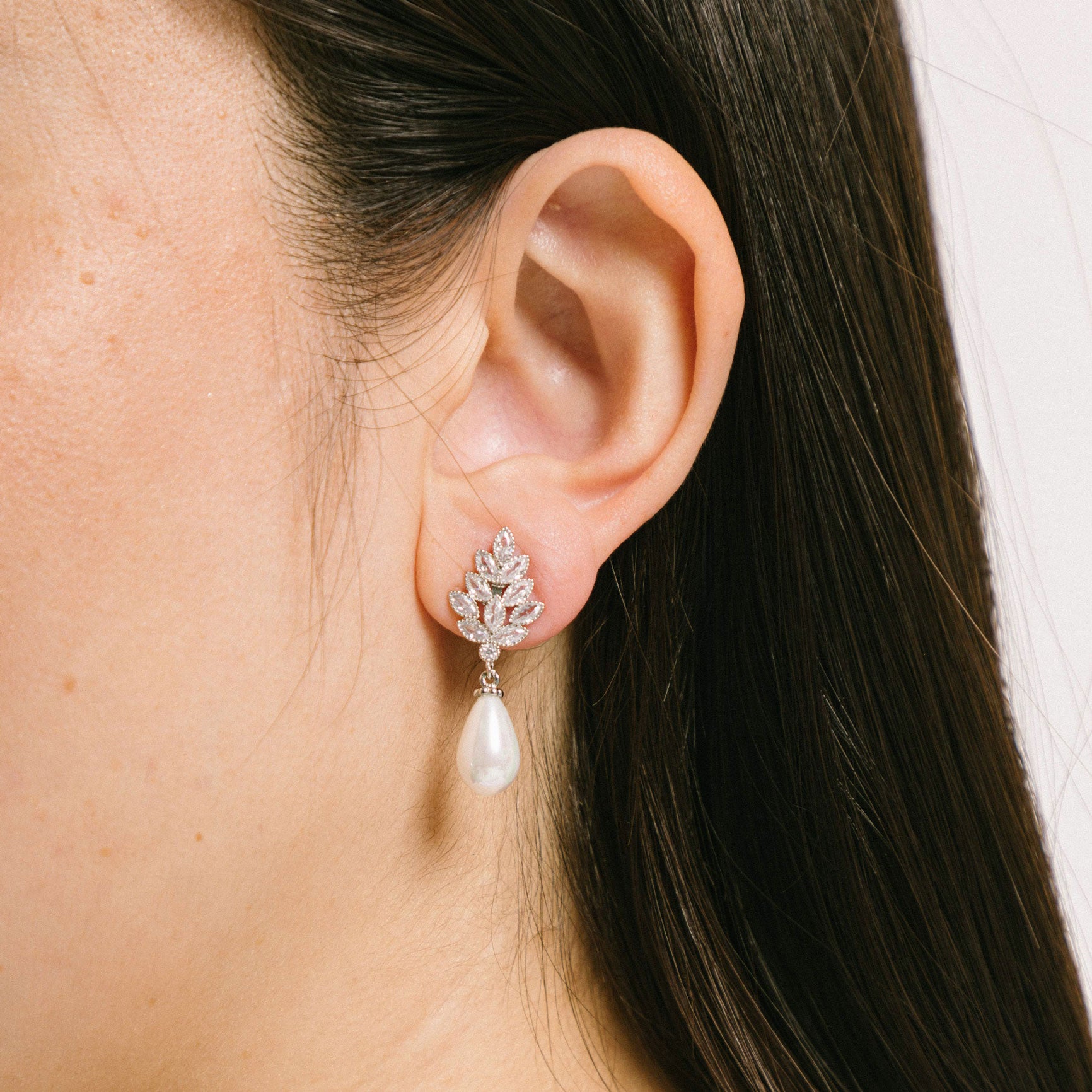 A model wearing the Madeline Clip On Earrings feature comfortable, secure and stylish padded clips ideal for all ear types. With a strong, consistent hold that can last up to 8-12 hours, they feature silver plated copper alloy with Cubic Zirconia and Simulated Pearl accents. This product is sold singularly as one pair.