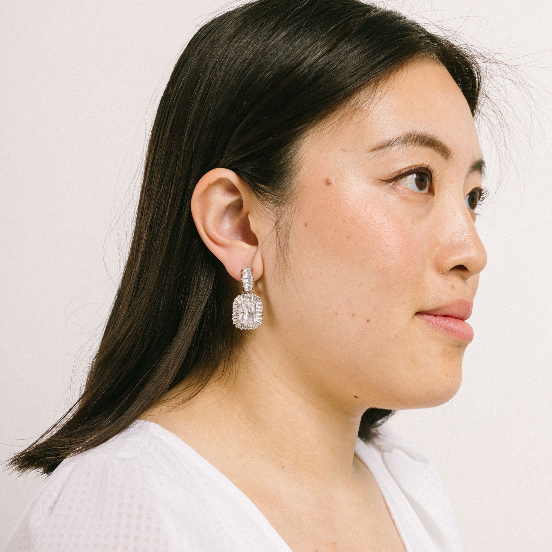 A model wearing the Quinn Clip On Earrings feature a secure padded clip-on closure, perfect for all types of ears, from thick and large to thin and sensitive. Enjoy hours of comfortable wear, up to 12 hours. Unable to be adjusted, this one pair of earrings are crafted of Silver plated copper alloy with Cubic Zirconia and are Lead/Nickel/Cadmium free. The clip-on feature includes removable rubber padding.