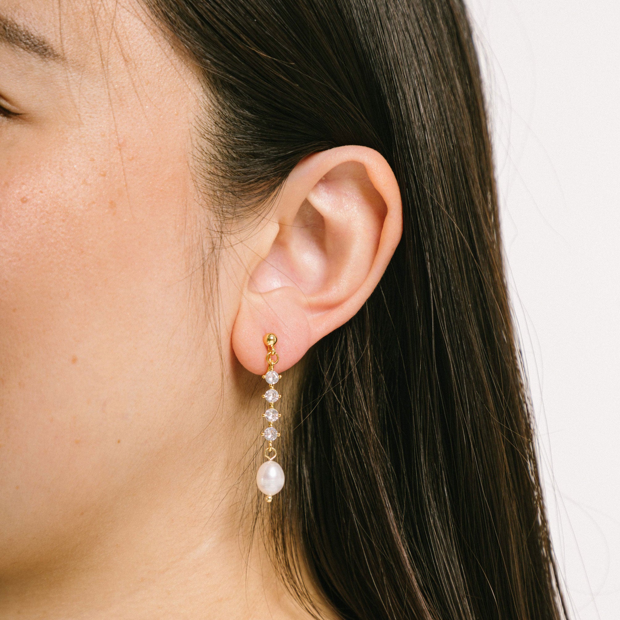 A model wearing the Sophia Clip On Earrings are designed for thick/large ears and sensitive ears alike. These earrings feature mosquito coil clip-on closures with a 24-hour average comfortable wear duration. Their medium secure hold can be adjusted gently by squeezing the padding forward once on the ear. Crafted with 14K gold plating, simulated faux pearl, and cubic zirconia, these earrings are lead/nickel/cadmium free and sold in single pairs.