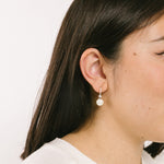 A model wearing the Claire Pearl Clip On Earrings in Silver present a mosquito coil clip-on closure crafted to accommodate all ear types—from thick/large to sensitive, from small/thin to stretched/healing—ensuring a comfortable fit. Intricately constructed from silver tone copper alloy, Cubic Zirconia, and Simulated Faux Pearl, these earrings add a sophisticated touch to any ensemble.