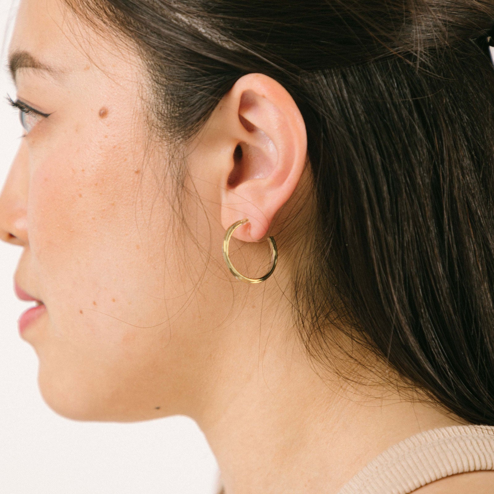 A model wearing the Gold Cassie Hoop Clip-On Earrings feature a resin closure, making them ideal for all ear types, including thick/large ears, sensitive ears, small/thin ears, and stretched/healing ears. On average, pairs are comfortably worn for 8-12 hours with a medium secure hold, and they are not adjustable. This item is sold as a single pair and is also available in Silver. The earrings are constructed with gold-tone metal alloy.