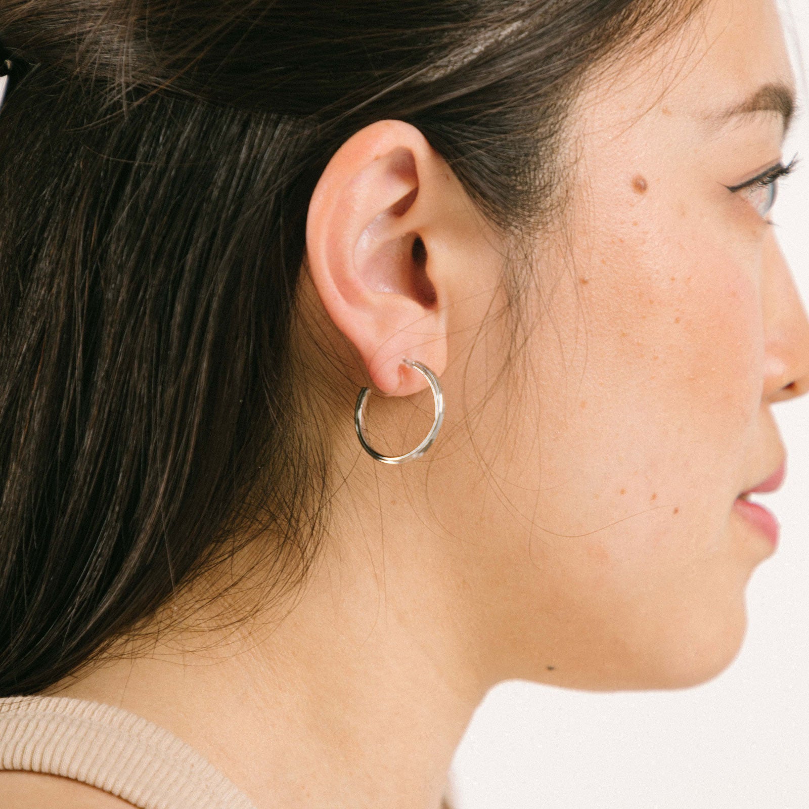 A model wearing the Silver Cassie Hoop Clip-On Earrings have a resin clip-on closure type and are suitable for all ear types, from thick/large ears to small/thin ears and stretched/healing ears. On average, comfortably wear for 8-12 hours, with a medium secure hold. Unfortunately, these earrings are unable to be adjusted. Offered in Silver Tone metal alloy, the earrings also come in Gold.