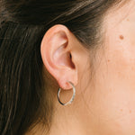 A model wearing the Silver Cassie Hoop Clip-On Earrings have a resin clip-on closure type and are suitable for all ear types, from thick/large ears to small/thin ears and stretched/healing ears. On average, comfortably wear for 8-12 hours, with a medium secure hold. Unfortunately, these earrings are unable to be adjusted. Offered in Silver Tone metal alloy, the earrings also come in Gold.
