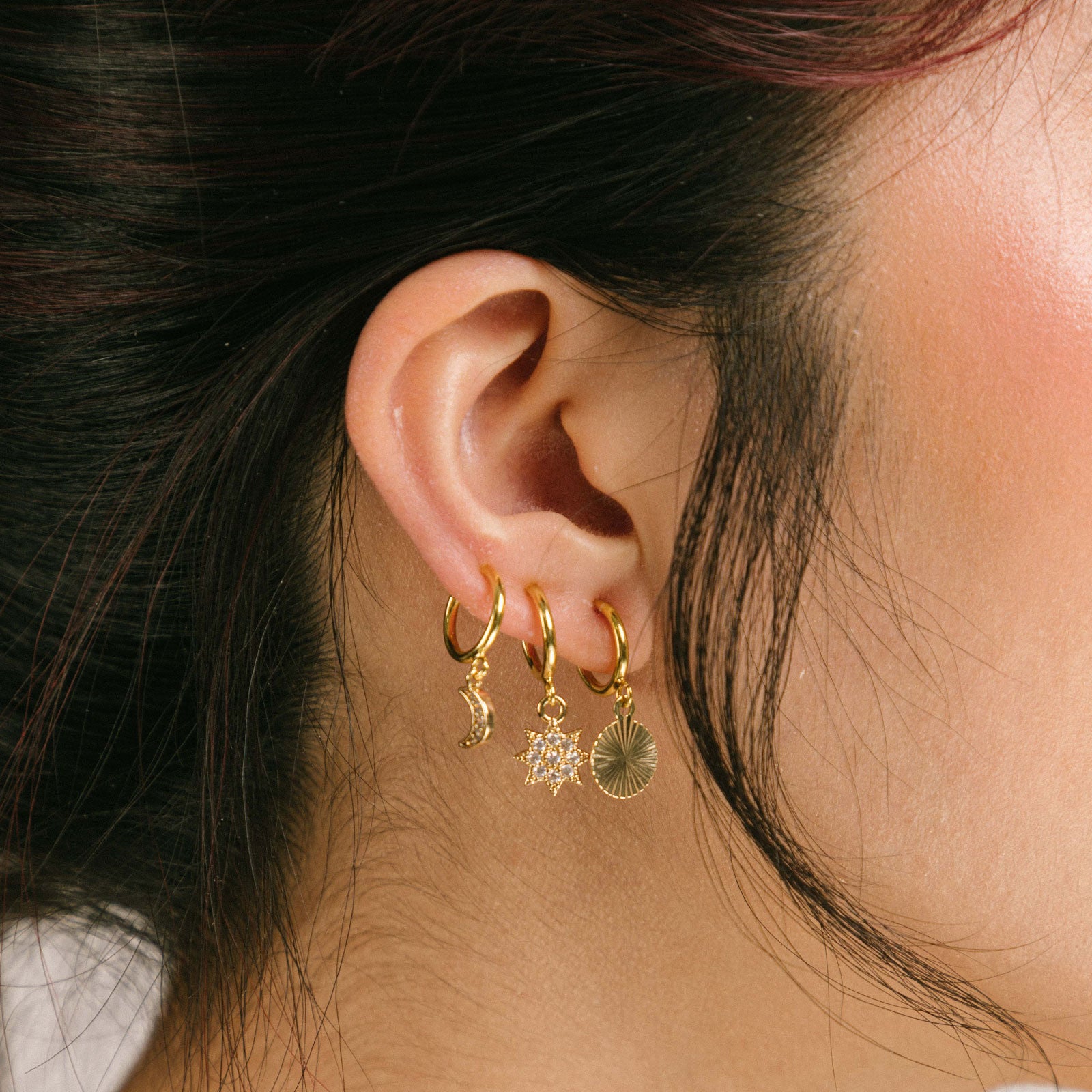 A model wearing Celestial Earrings Stack Set, particularly suited to those with delicate or slender earlobes. Expertly crafted from brass and punctuated with glimmering cubic zirconias, this set features the Sunbeam Clip On Earrings, Star Charm Clip On Earrings, and Moon Charm Clip On Earrings.