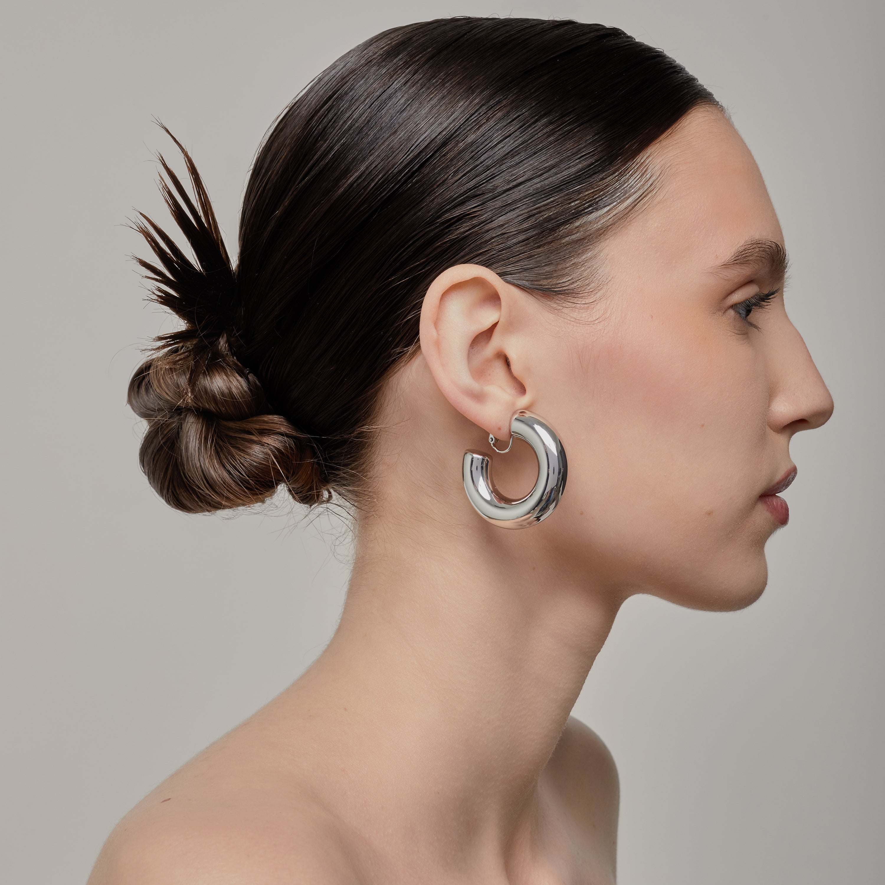 A model wearing the Chunky Hoop Clip On Earrings in Silver. With a secure screwback closure, these earrings are suitable for a variety of ear sizes, including sensitive and keloid-prone ears. Designed for long-lasting wear and can be manually adjusted for a perfect fit. Note: includes one pair.