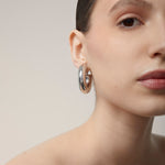 A model wearing the Chunky Hoop Clip On Earrings in Silver. With a secure screwback closure, these earrings are suitable for a variety of ear sizes, including sensitive and keloid-prone ears. Designed for long-lasting wear and can be manually adjusted for a perfect fit. Note: includes one pair.