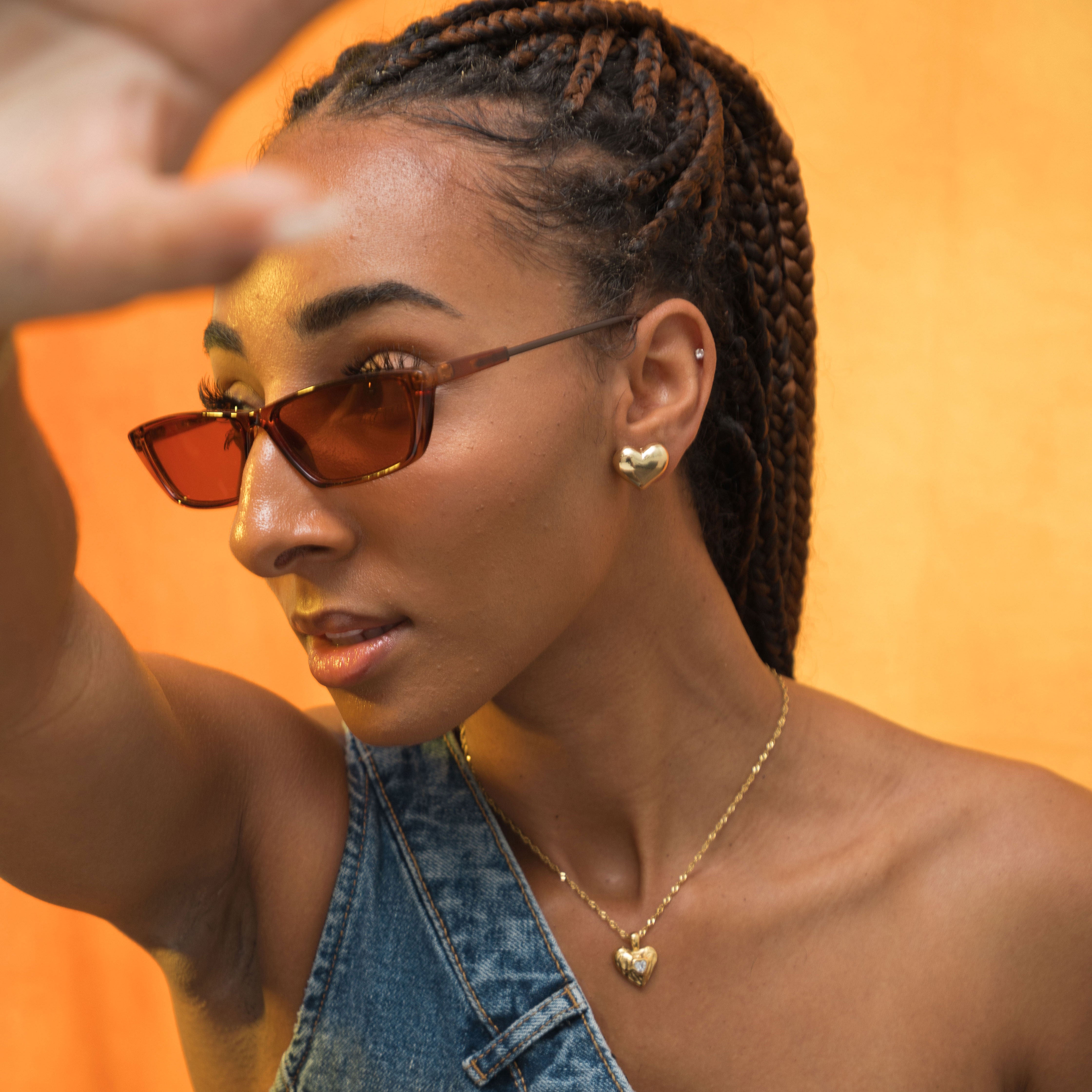 A model wearing the Coeur Clip On Earrings in Gold offer a medium-strength, adjustable hold via a mosquito coil clip. Ideal for all ear types, these earrings provide a secure yet comfortable fit for up to 24 hours. Crafted with Zinc Alloy and Copper, each purchase contains a single pair.