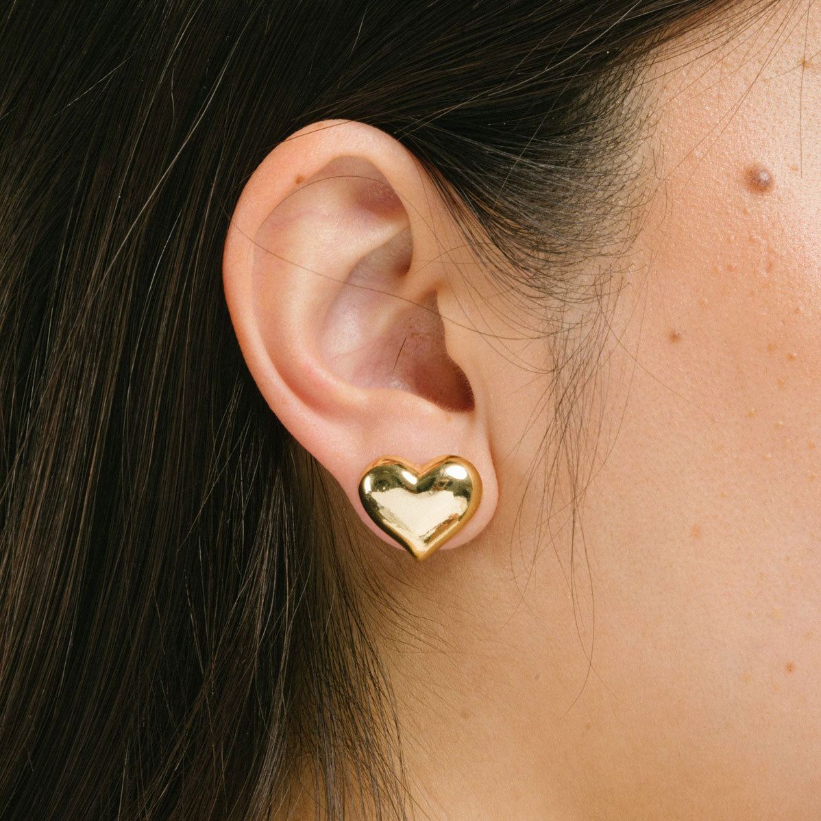 A model wearing the Coeur Clip On Earrings in Gold offer a medium-strength, adjustable hold via a mosquito coil clip. Ideal for all ear types, these earrings provide a secure yet comfortable fit for up to 24 hours. Crafted with Zinc Alloy and Copper, each purchase contains a single pair.