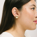 A model wearing the Coeur Clip On Earrings in Gold offer a medium-strength, adjustable hold via a mosquito coil clip. Ideal for all ear types, these earrings provide a secure yet comfortable fit for up to 24 hours. Crafted with Zinc Alloy and Copper, each purchase contains a single pair.